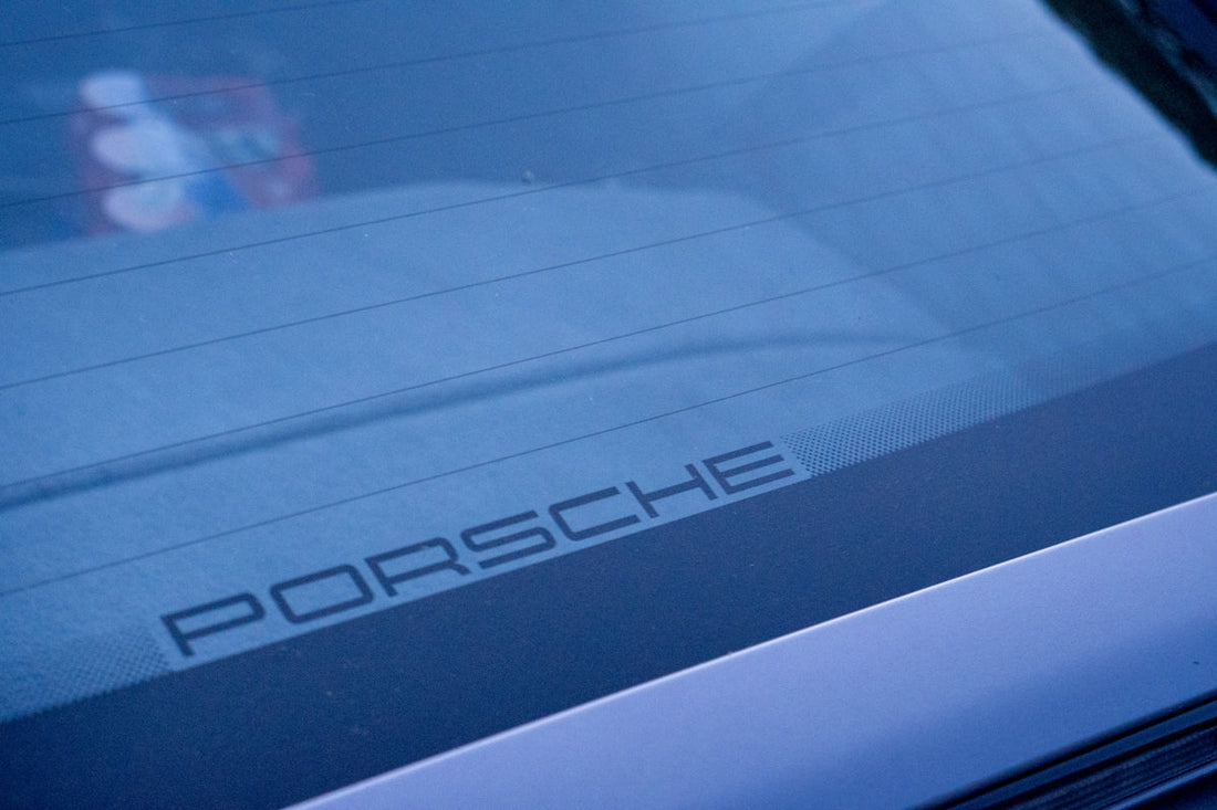 Close-up of Porsche rear windshield with logo, luxury car detail visible