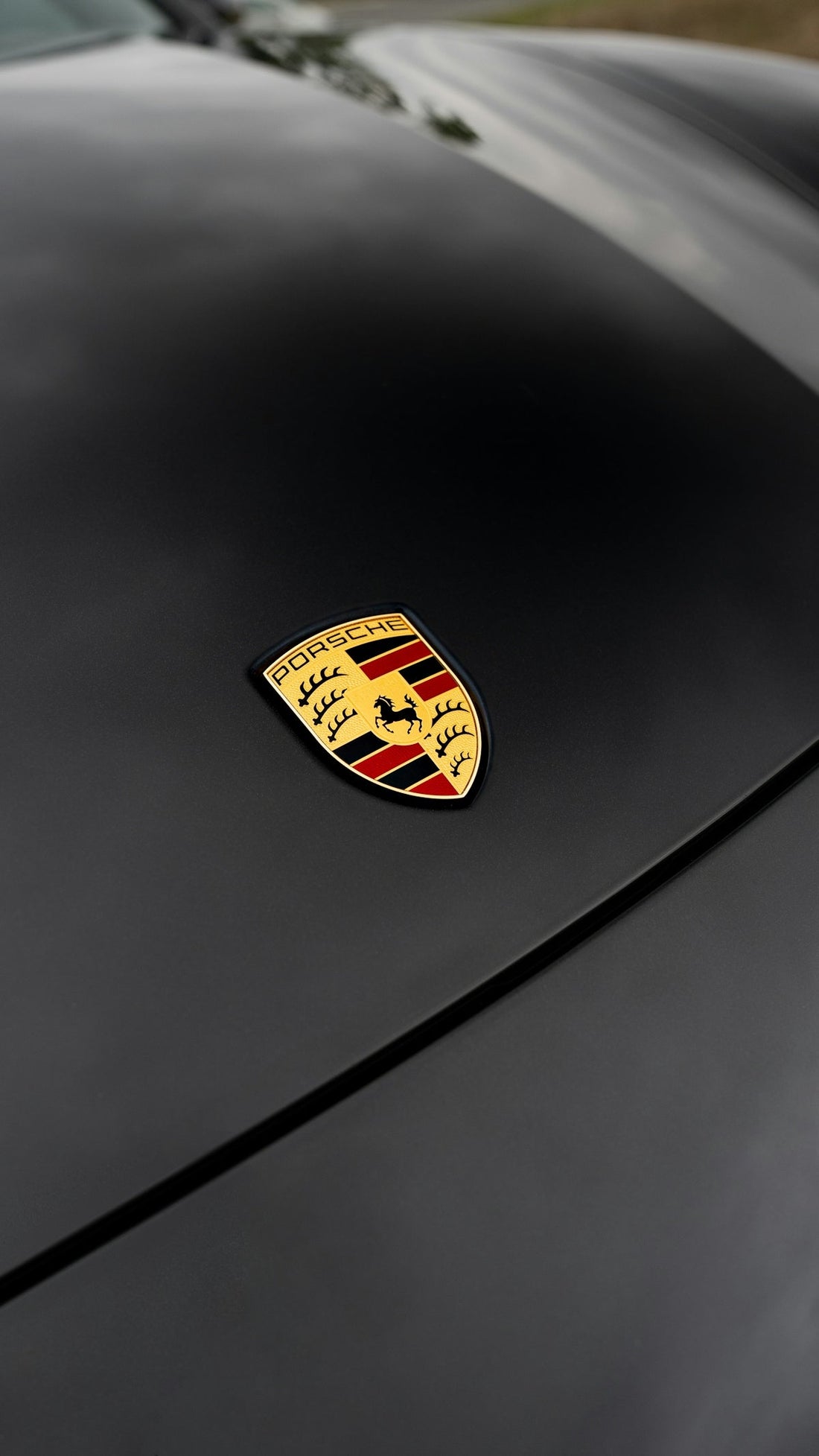Porsche emblem on matte black luxury car hood, close-up, exotic supercar detail