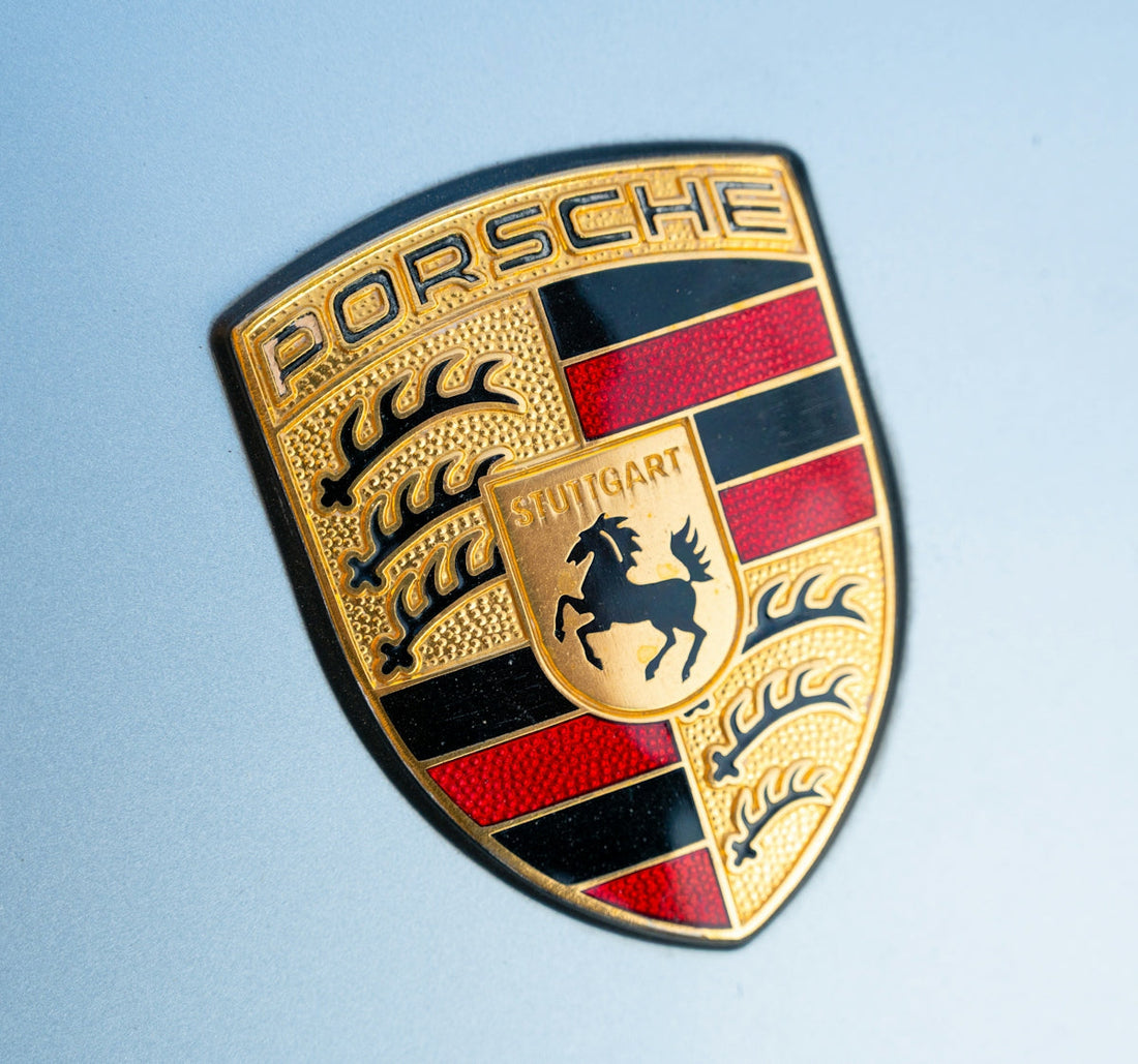 Porsche emblem close-up on silver car hood, luxury sports car badge, exotic vehicle logo
