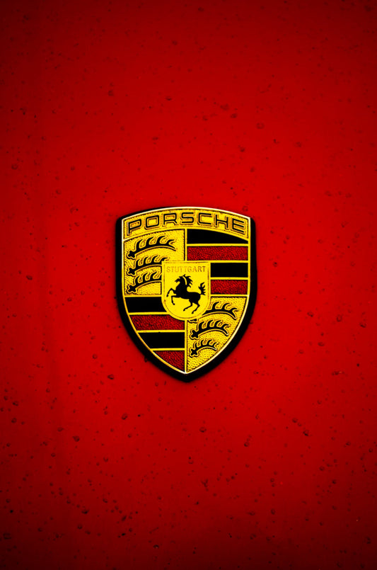 Porsche crest emblem on red car hood, close-up, luxury sports car badge
