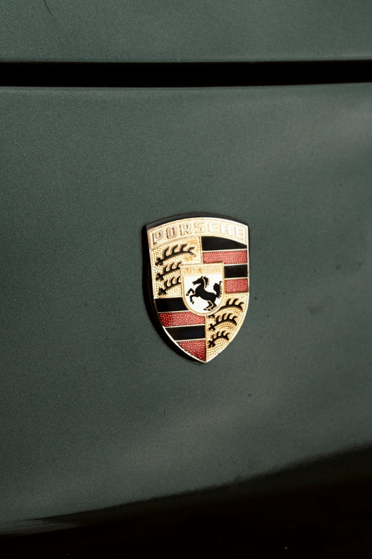 Close-up of Porsche emblem on a dark green exotic car hood