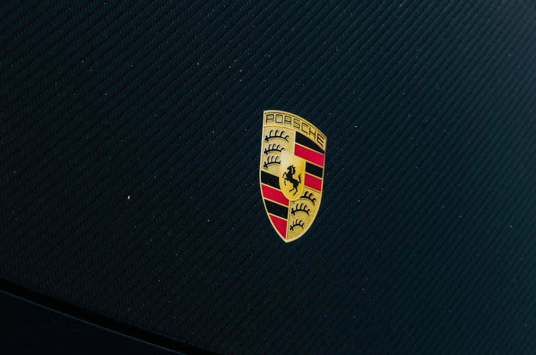 Close-up of Porsche logo on black carbon fiber car hood, luxury sports car detail