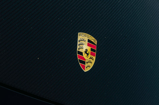 Close-up of Porsche logo on black carbon fiber car hood, luxury sports car detail