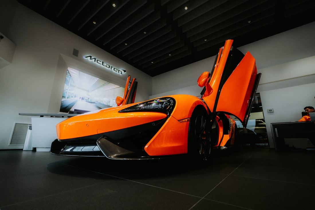 Orange McLaren supercar with butterfly doors open in showroom, luxury exotic car display