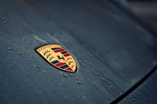 Close-up of Porsche badge on wet hood, luxury car emblem with water droplets