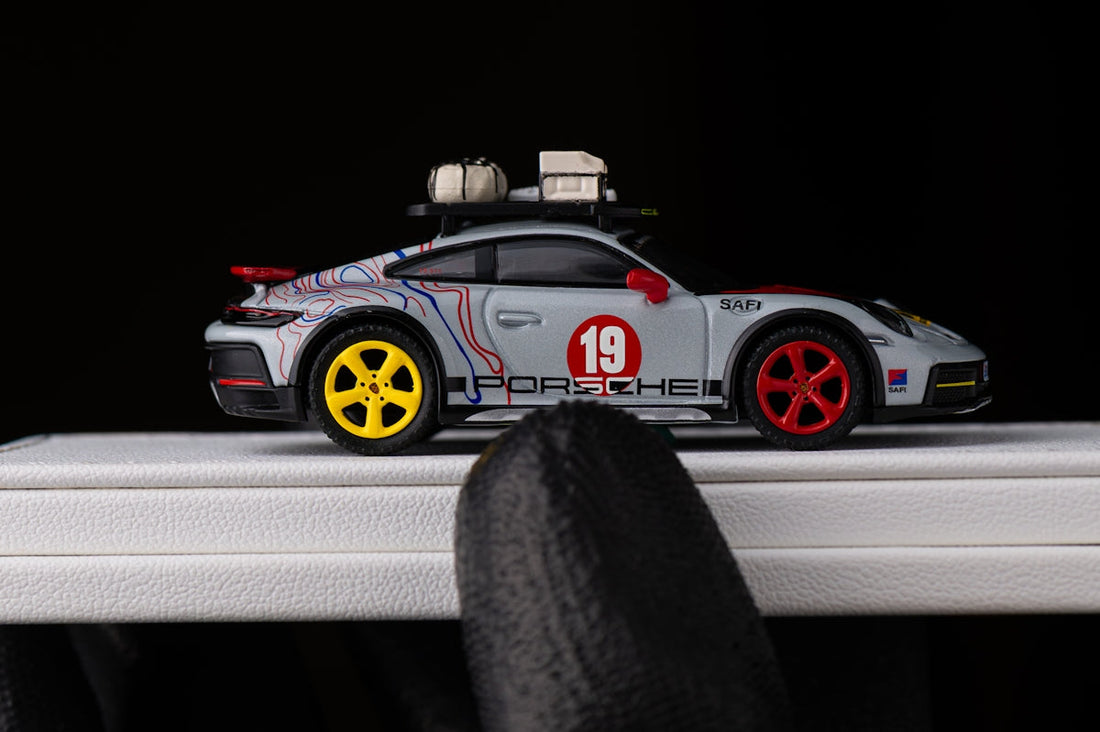 Diecast Porsche model car with roof cargo, racing livery, and mismatched wheels