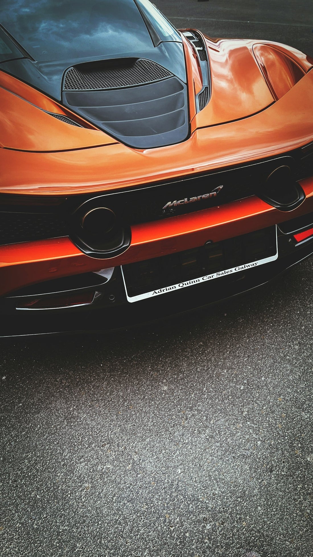 Close-up of orange McLaren supercar rear with dual exhaust and license plate, parked on asphalt