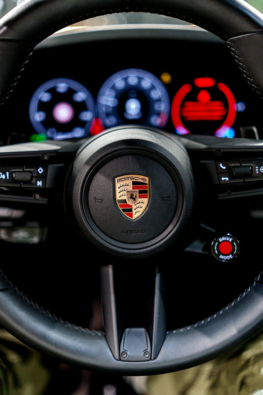 Close-up of a porsche steering wheel with illuminated dashboard.